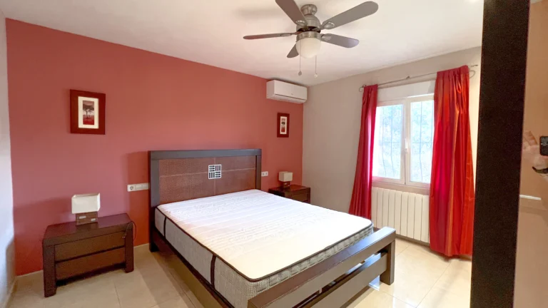 Bedroom with red accent wall, ceiling fan and large window in Maryvilla