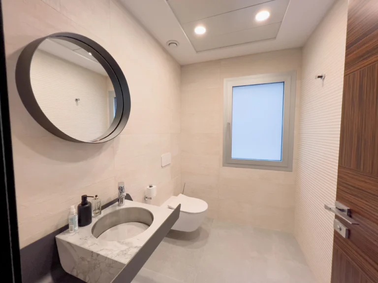 Modern minimalist guest bathroom with round mirror and wall-mounted toilet