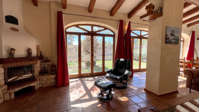 Rustic lounge with fireplace and large arched windows opening to garden views