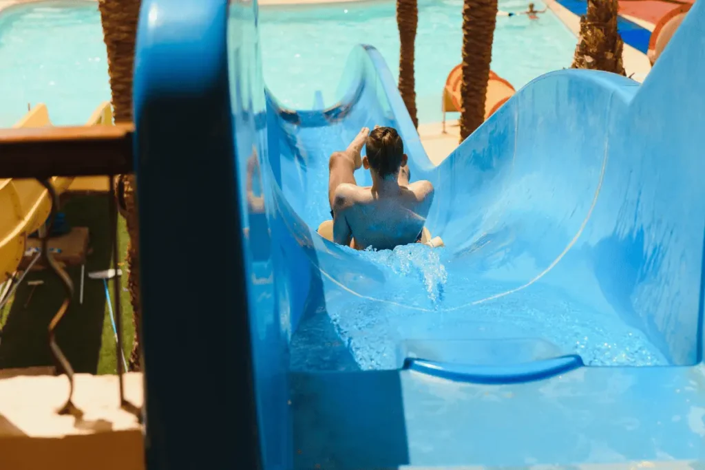 Back view of a child sliding down a bright blue water slide at a water park near Calpe, illustrating family fun and summer activities on the Costa Blanca.
