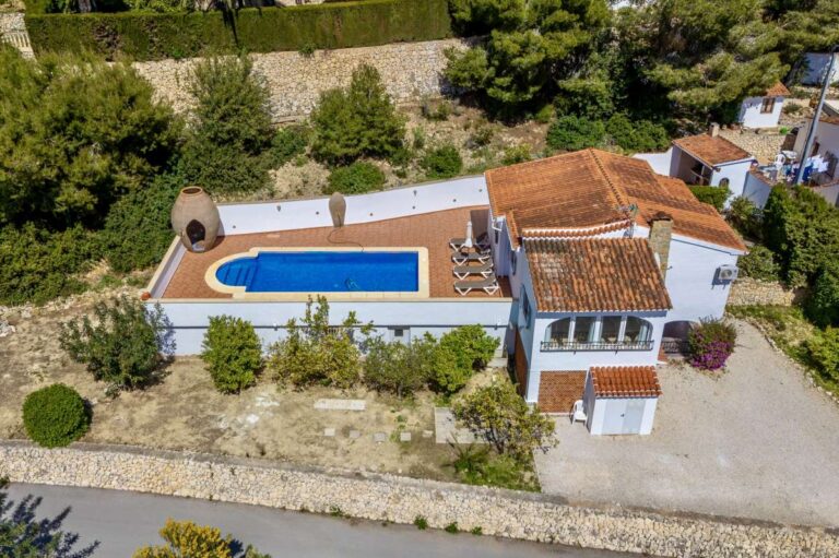 Aerial view of a charming Benissa Coast villa with private pool, spacious plot, gravel driveway, garden areas and surrounding greenery
