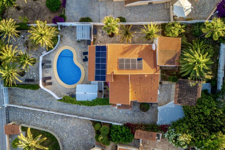 Aerial view of a renovated villa in Moraira with private pool, solar panels, roof terrace, palm trees and surrounding garden areas