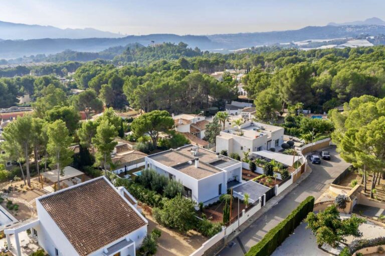 Aerial view of a single-level modern villa in Santa Clara, Altea with surrounding residential area, trees, mountain views and Mediterranean landscape