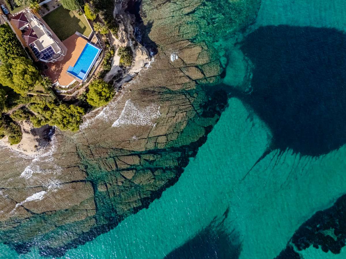 Aerial view of Cala Bassetes and turquoise Mediterranean water beside a frontline villa in Les Bassetes.