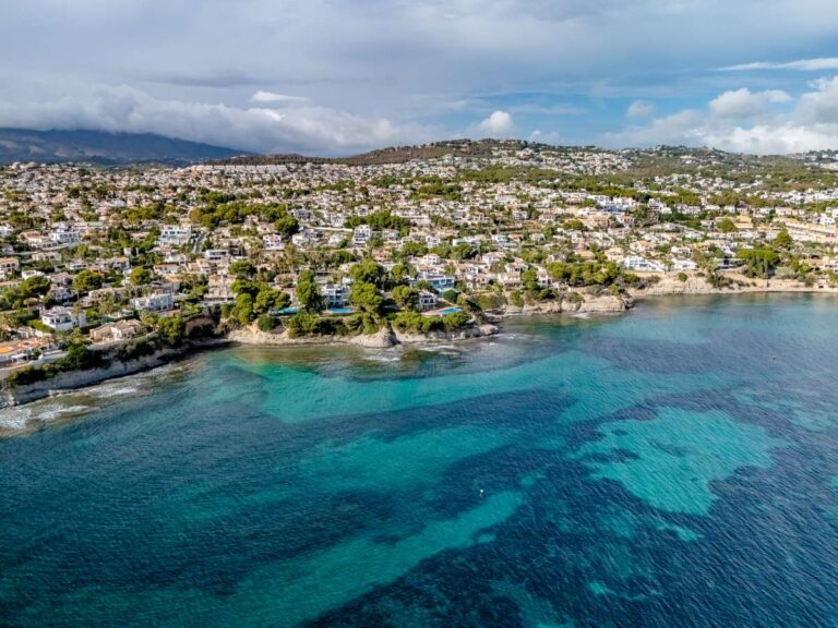 Aerial view of the Les Bassetes coastline with turquoise Mediterranean water near a frontline villa in Benissa Coast.