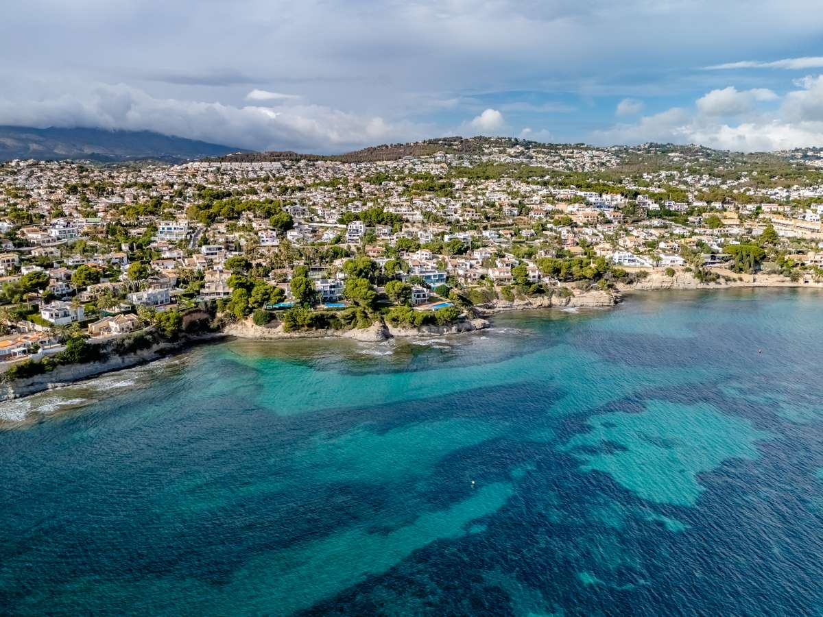 Aerial view of the Les Bassetes coastline with turquoise Mediterranean water near a frontline villa in Benissa Coast.