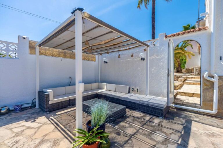 Alt text: Covered outdoor seating area at a renovated single-level villa in Moraira with pergola, built-in seating, stone terrace and garden access