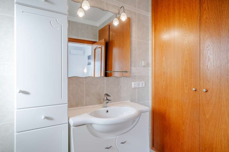 Bathroom inside a Calpe villa with sink, mirror, storage cabinet and wooden door
