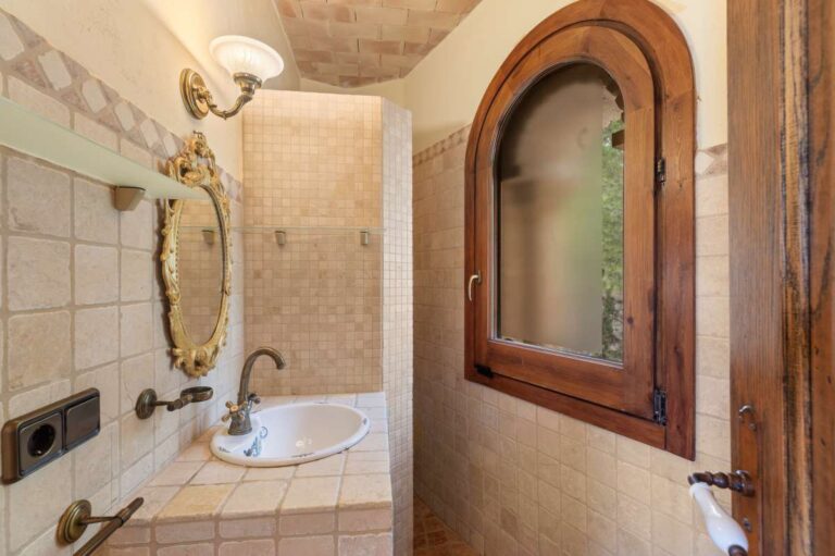 Bathroom inside a finca-style villa in Benissa Costa with arched window, bath, tiled walls, vanity unit and rustic Mediterranean finish