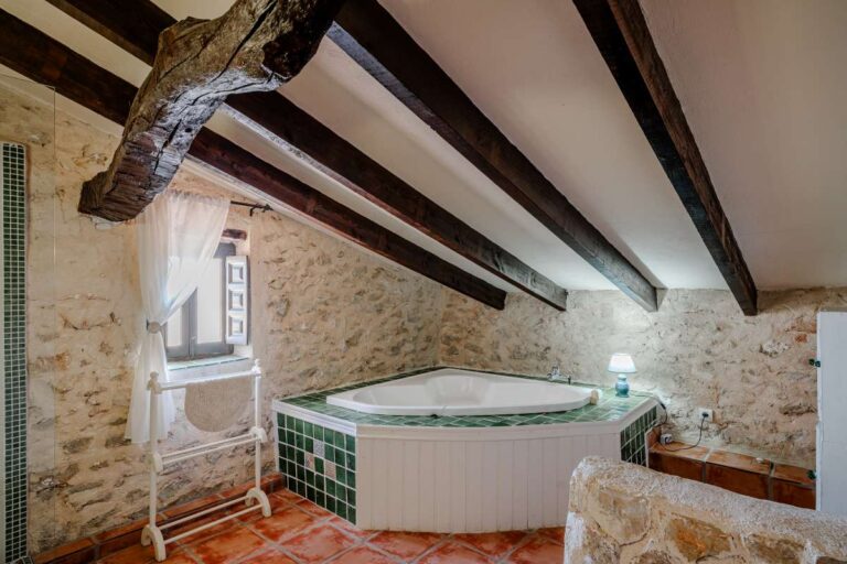 Bathroom inside a historic finca in Benissa with jacuzzi bath, exposed stone walls, wooden beams and traditional tiled flooring