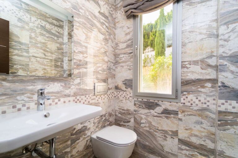 Bathroom inside a luxury villa in Calpe with stone-effect tiled walls, toilet, basin and natural light from the window