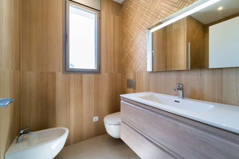 Badezimmer in einer neu gebauten Luxusvilla in der Nähe des Yachthafens Puerto Blanco in Calpe mit Wandverkleidung in Holzoptik, großem Waschtisch, Bidet und modernem Spiegel