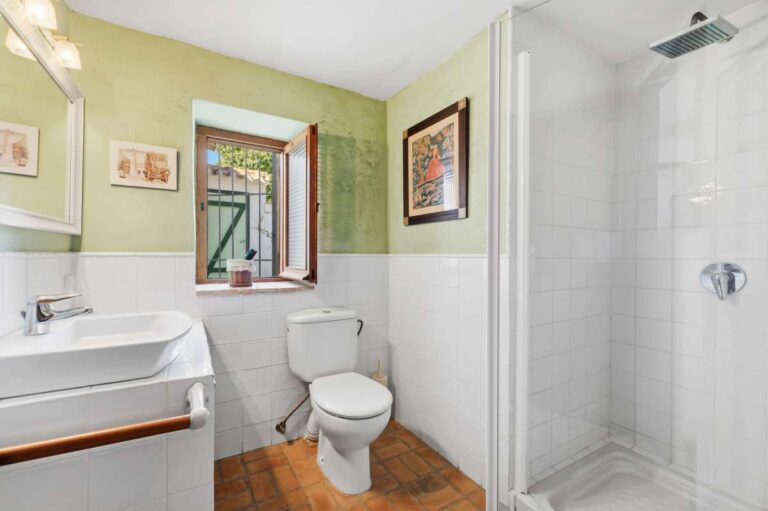 Bathroom inside a traditional Spanish finca near Moraira with shower enclosure, toilet, vanity unit, tiled walls and window