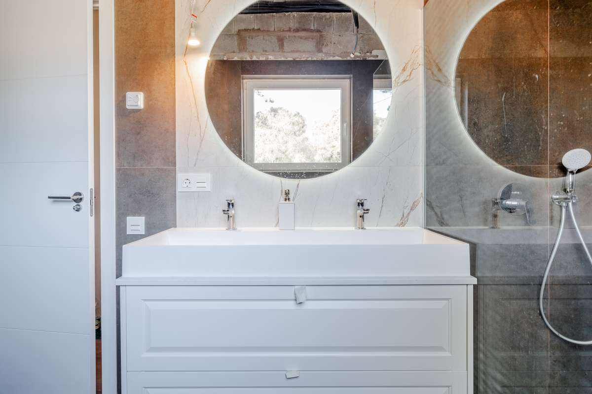 Bathroom vanity with round mirror and walk-in shower inside a new build villa for sale in Calpe