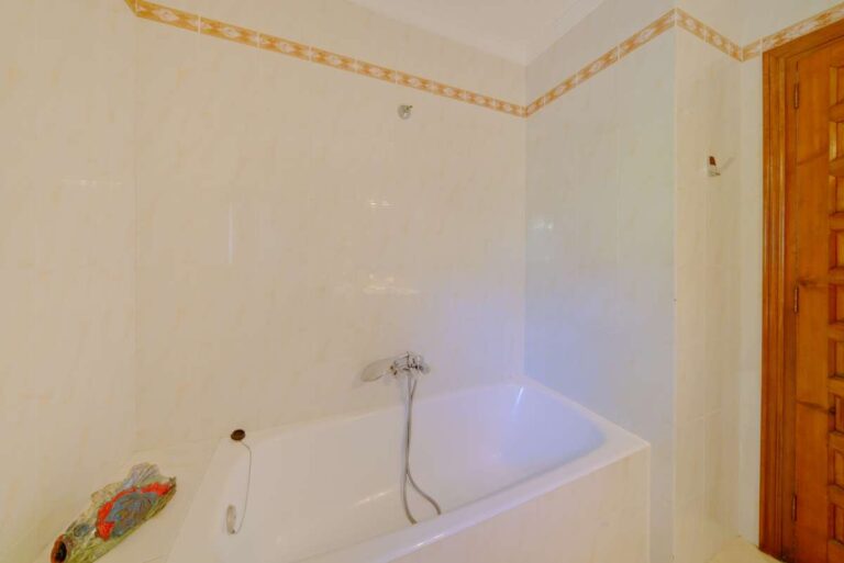 Bathroom with bath, tiled walls and wooden door inside a Mediterranean villa near Puerto Blanco in Calpe.
