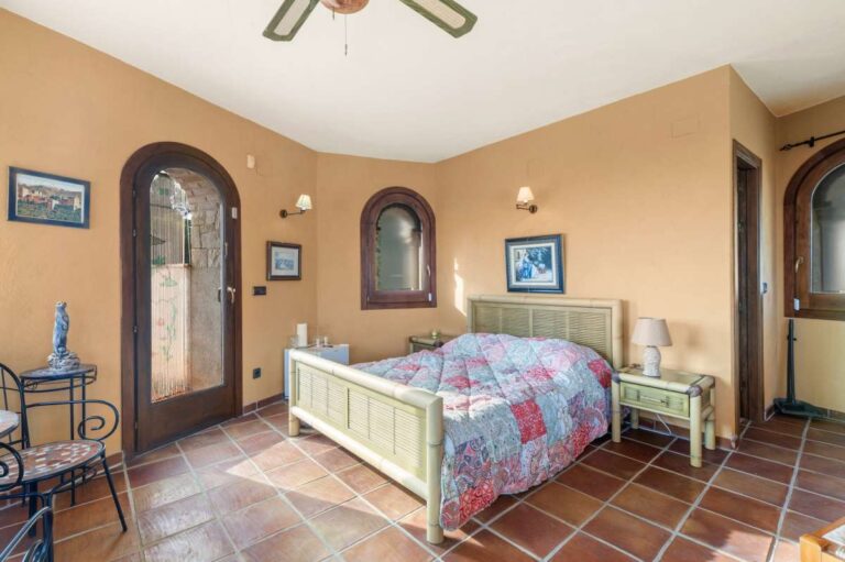 Bedroom inside a finca-style villa in Benissa Costa with terracotta tiled floor, arched window, wooden furniture and rustic Mediterranean character