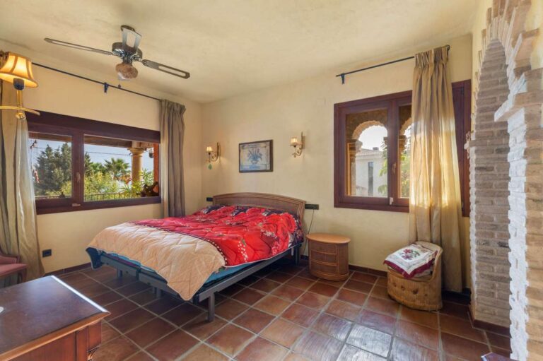 Bedroom inside a finca-style villa in Benissa Costa with terracotta tiled floor, ceiling fan, wooden furniture and garden views through the window