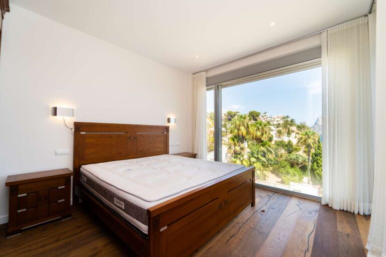 Bedroom inside a luxury villa in Calpe with wood flooring, terrace access, fitted curtains and natural light