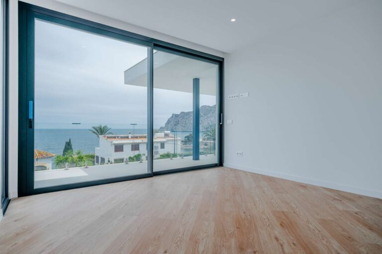 Bedroom inside a modern second-line sea villa in La Calalga, Calpe with large sliding windows, sea views and wood flooring