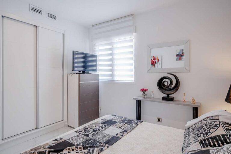 Bedroom inside a renovated apartment by Arenal-Bol Beach in Calpe with fitted wardrobe, TV, natural light and modern white interior