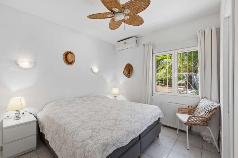 Bedroom inside a renovated single-level villa in Moraira with garden views, air conditioning, ceiling fan and bright neutral interior