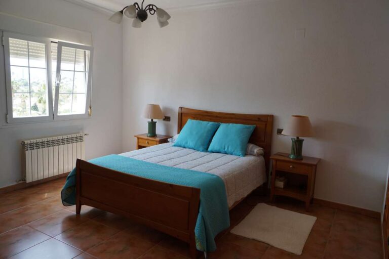 Bedroom with blue bed, natural light and traditional furniture inside a Mediterranean villa near La Calalga Beach in Calpe.