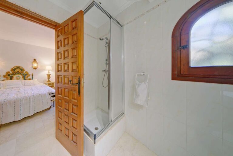 Bedroom with en-suite shower room and traditional wooden door inside a Mediterranean villa near Puerto Blanco in Calpe.