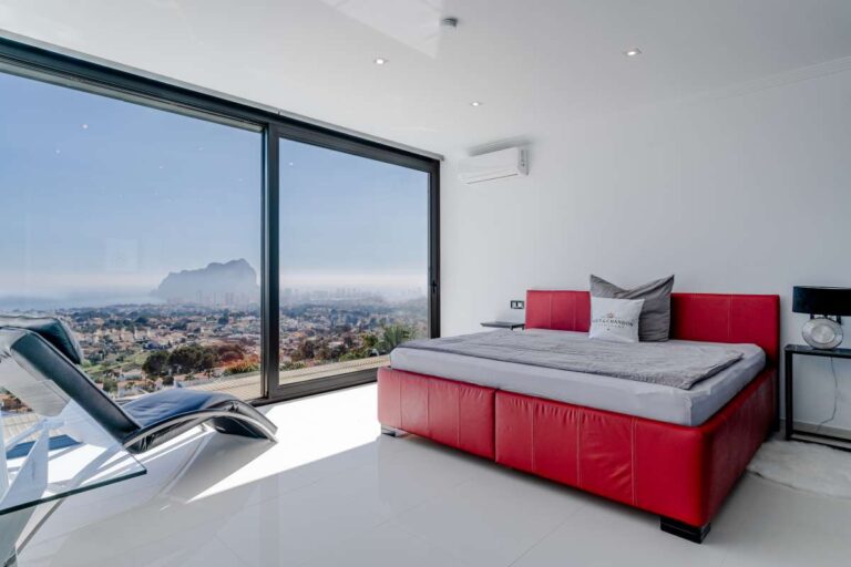 Bedroom with red bed, large window and panoramic sea views towards the Peñón de Ifach inside a luxury villa in Gran Sol, Calpe.