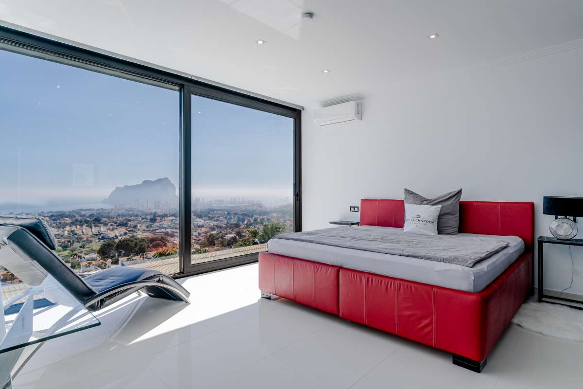Bedroom with red bed, large window and panoramic sea views towards the Peñón de Ifach inside a luxury villa in Gran Sol, Calpe.