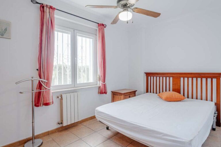 Bedroom with wooden bed frame, ceiling fan and natural light inside a Mediterranean villa in Calpe.