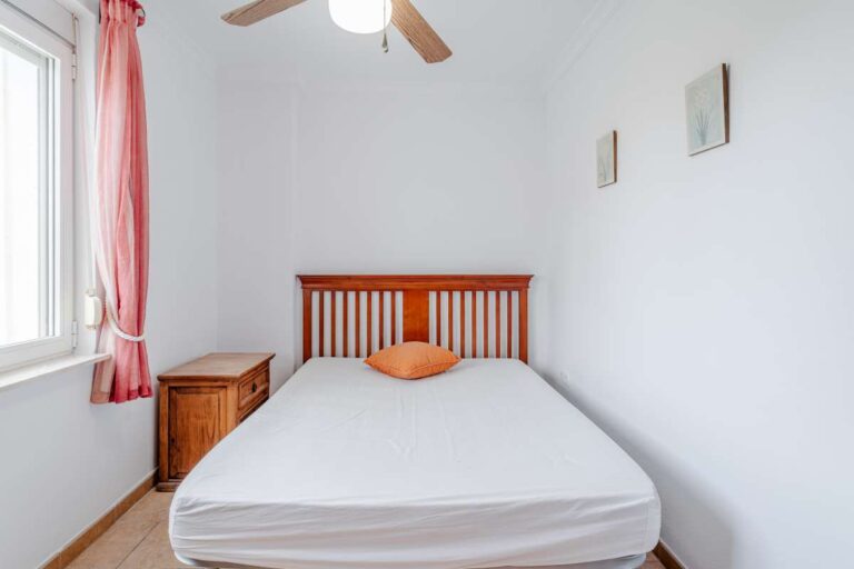 Bedroom with wooden bed frame, ceiling fan and natural light inside a Mediterranean villa with independent guest accommodation in Calpe.