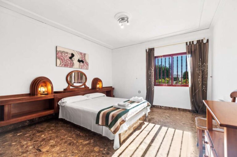 Bedroom with wooden bed frame, dresser and natural light inside a spacious villa with guest apartments in Calpe.