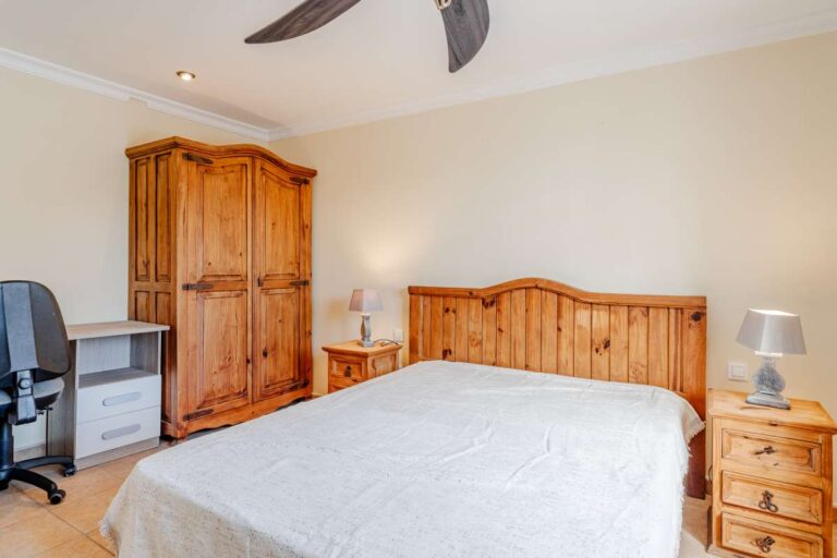 Bedroom with wooden bed frame, wardrobe, bedside tables and ceiling fan inside a Mediterranean villa with guest accommodation in Calpe.