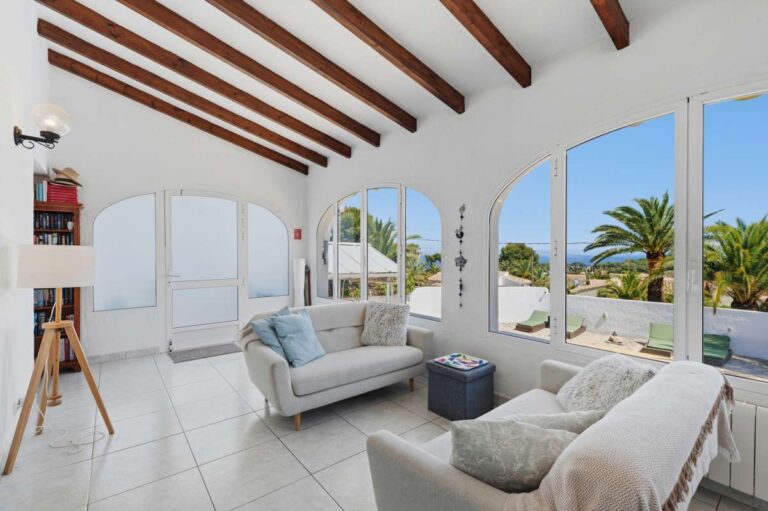 Bright living room inside a renovated single-level villa in Moraira with beamed ceiling, sofa seating, arched windows and garden views