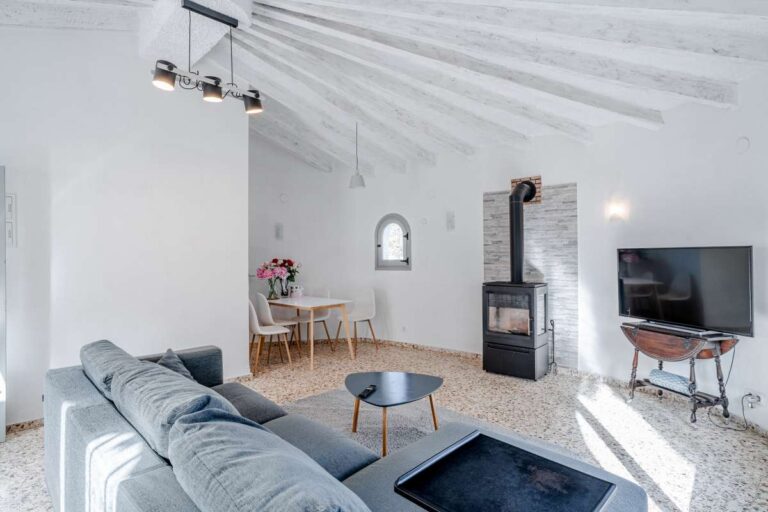 Bright living room with sofa, fireplace, arched window and beamed ceiling inside a Mediterranean villa in Maryvilla, Calpe.