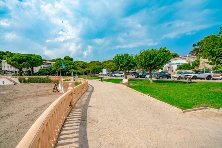 Coastal walkway near Les Platgetes Beach in Moraira with sandy beach, landscaped green area, trees and Mediterranean Sea views