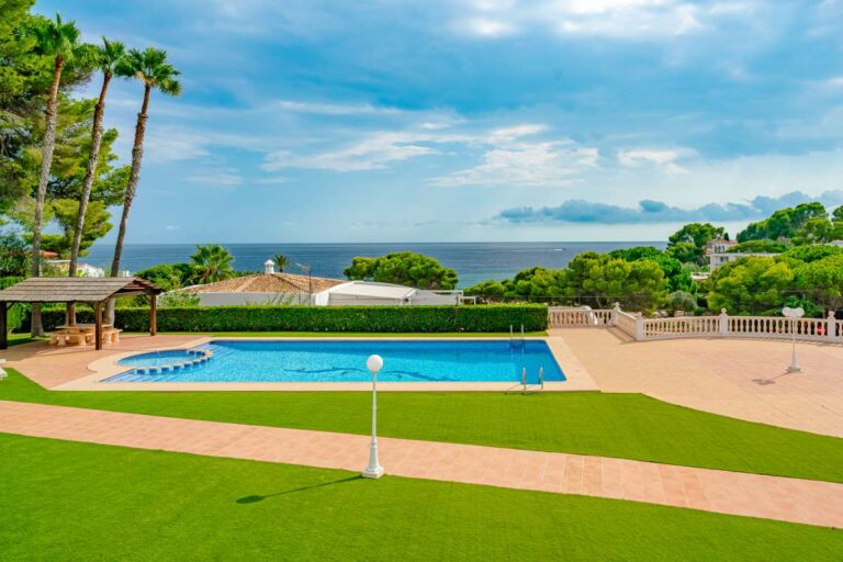 Communal swimming pool and landscaped gardens at a duplex apartment near Les Platgetes Beach in Moraira with sea views beyond