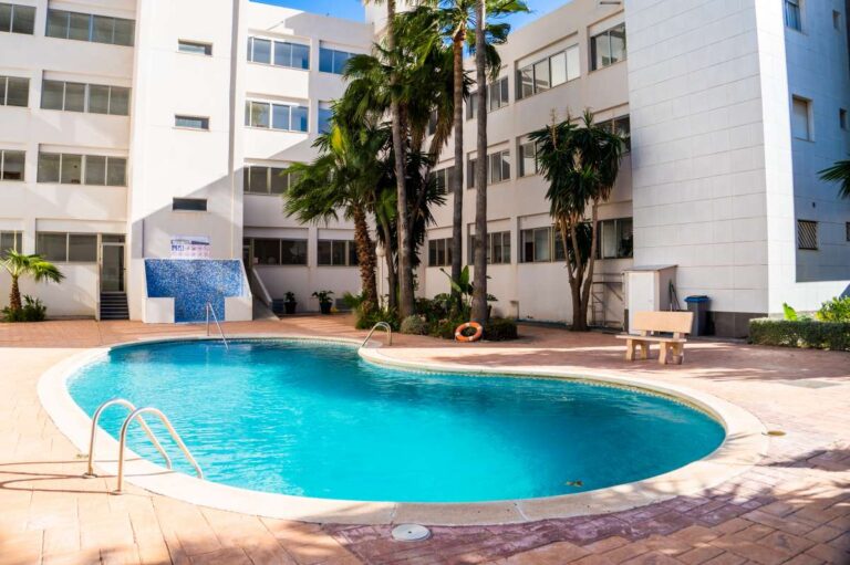 Communal swimming pool at a beachfront apartment building by La Fossa Beach in Calpe with palm trees, terrace area and surrounding apartments