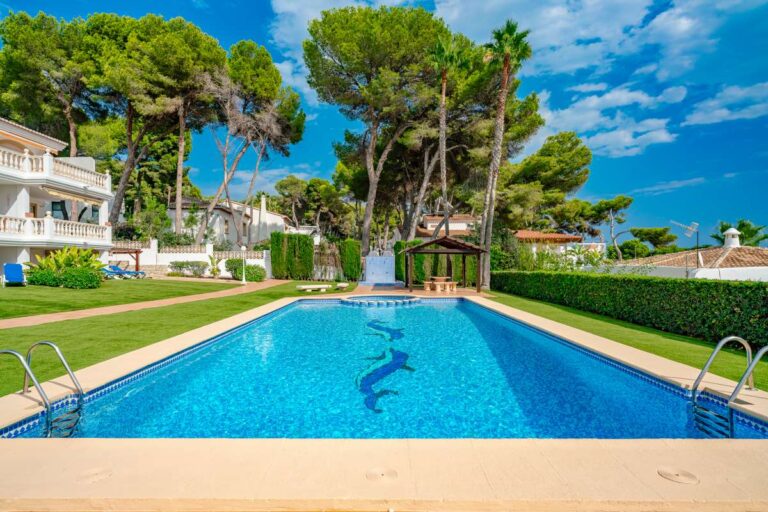 Communal swimming pool at a duplex apartment near Les Platgetes Beach in Moraira with landscaped gardens, pine trees and residential surroundings