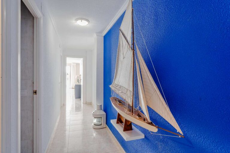 Corridor inside a beachfront apartment by La Fossa Beach in Calpe with nautical decoration, blue feature wall and access to living areas