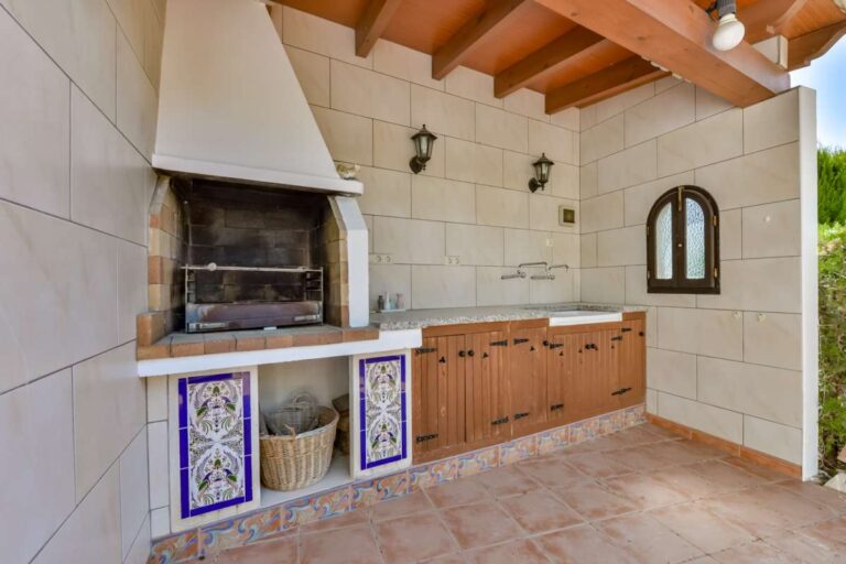 Covered barbecue kitchen at a charming Benissa Coast villa with built-in grill, tiled walls, wooden storage and traditional Mediterranean finish