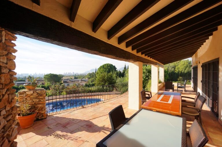 Covered dining terrace at a Mediterranean villa in Calpe with outdoor table, private pool views and mature garden surroundings