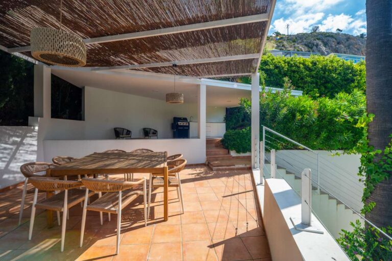 Covered dining terrace at a modern villa in Altea Hills with outdoor table, pergola, tiled floor and garden views