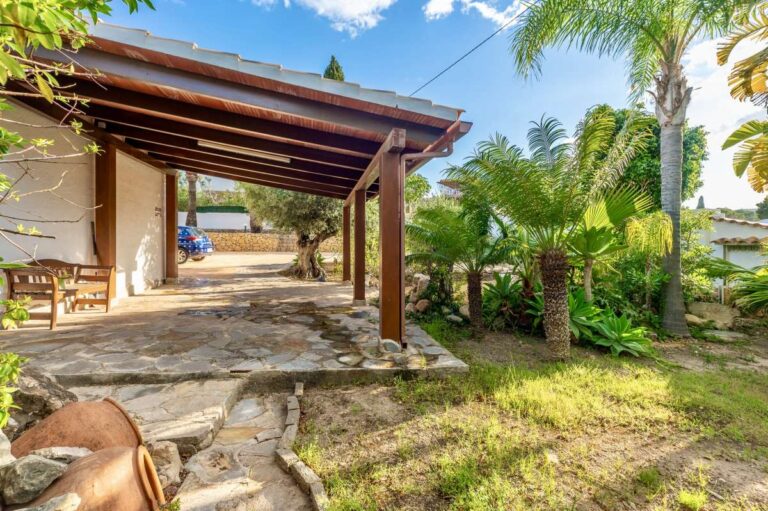 Covered outdoor area at a premium coastal villa on the Benissa Costa with timber pergola, stone terrace, garden planting and palm trees