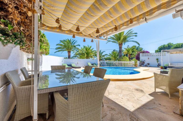 Covered outdoor dining area at a renovated single-level villa in Moraira with pool views, shaded terrace space and Mediterranean garden surroundings