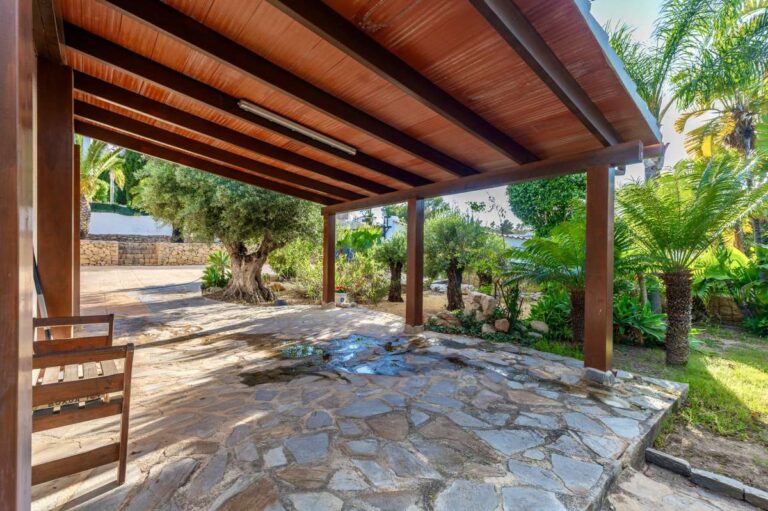 Covered parking area at a premium coastal villa on the Benissa Costa with timber pergola, stone paving and garden surroundings