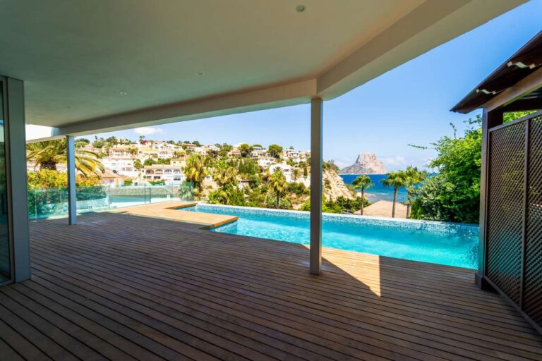 Covered pool terrace at a luxury villa in Calpe with infinity pool, wooden decking and panoramic sea views towards the Peñón de Ifach
