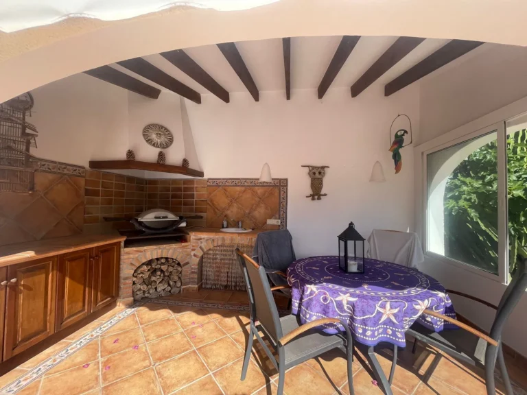 Covered summer kitchen and dining area with BBQ, tiled floor, and outdoor seating at a villa in Calpe.