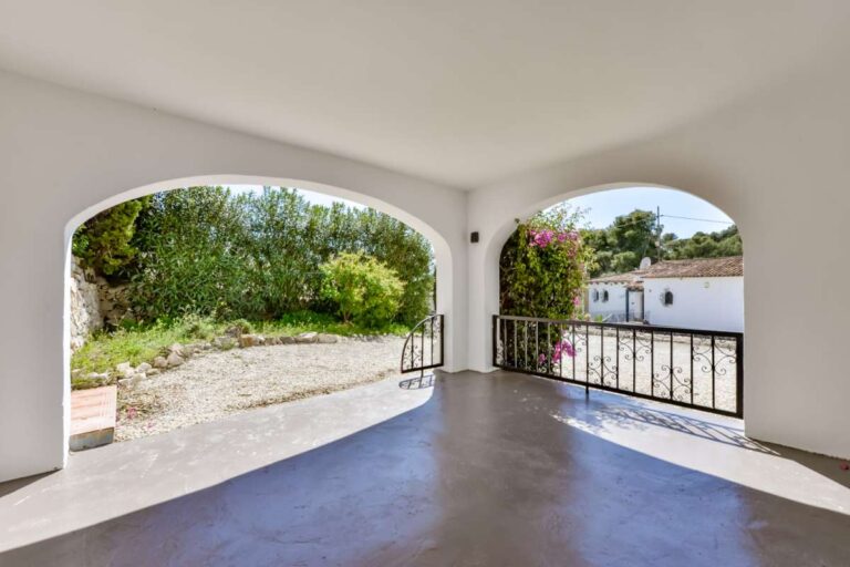 Covered terrace at a charming Benissa Coast villa with arched openings, garden views, tiled floor and Mediterranean outdoor space
