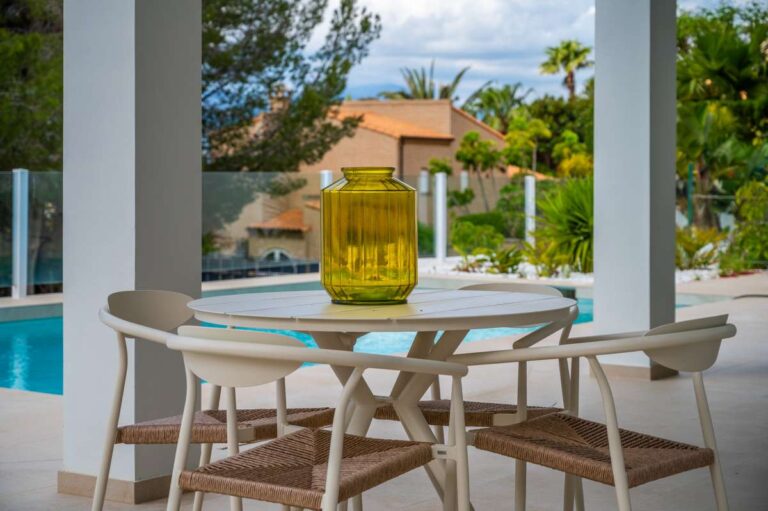Covered terrace dining area at a modern villa in Altea Hills with private pool views, outdoor table, glass railing and Mediterranean garden surroundings